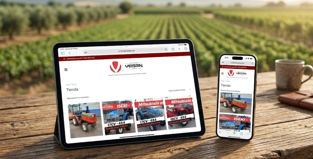 una tablet y un smartphone sobre una mesa de madera rústica; en las pantallas se ve claramente la web de Comercial Veisan con fotos de tractores. Al fondo, un campo de cultivo desenfocado.